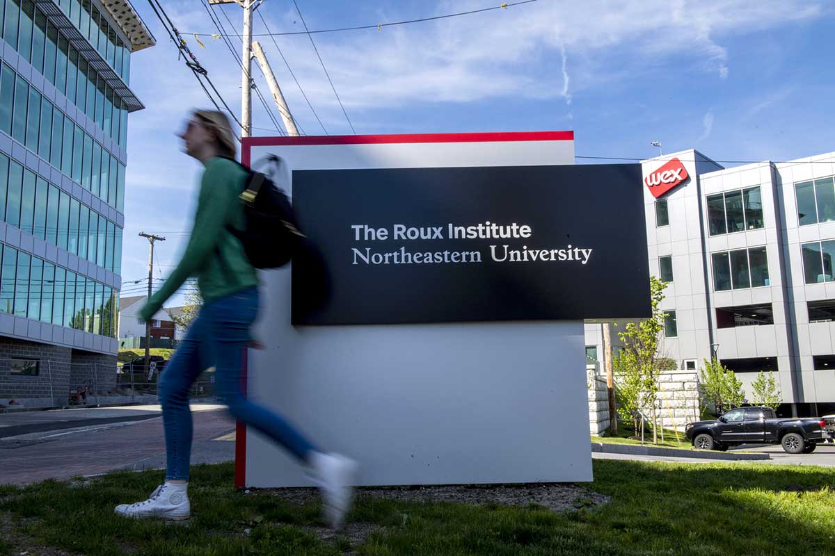 A student walks by a sign that says "Roux Institute - Northeastern University" at Northeastern's Portland campus