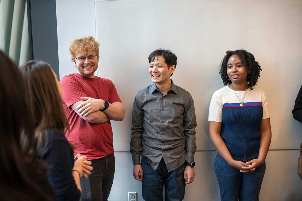 Four Khoury students and researchers smile while having a conversation in a classroom.