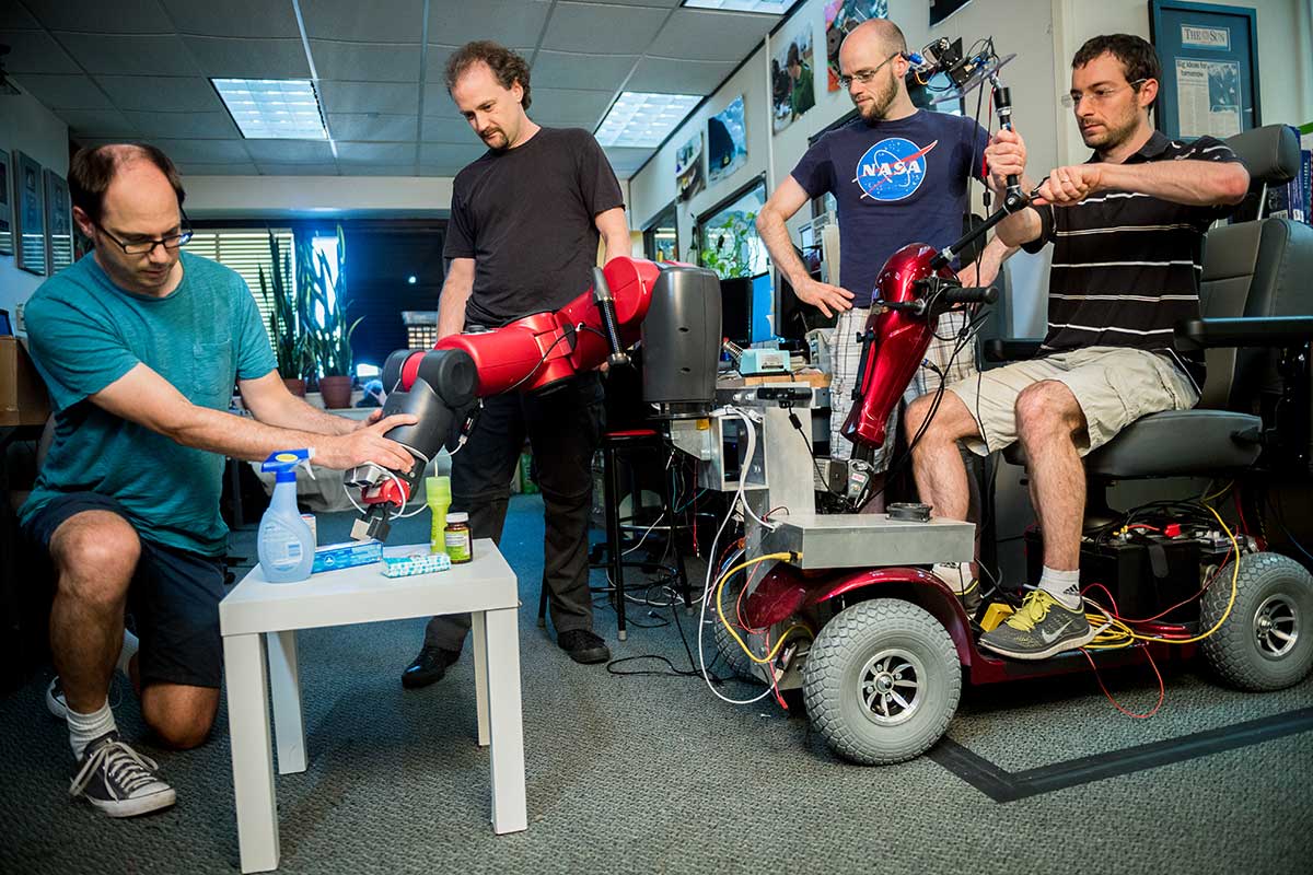 Four Khoury researchers test out a motorized scooter with a robotic arm. One of the researchers is sitting on the scooter.