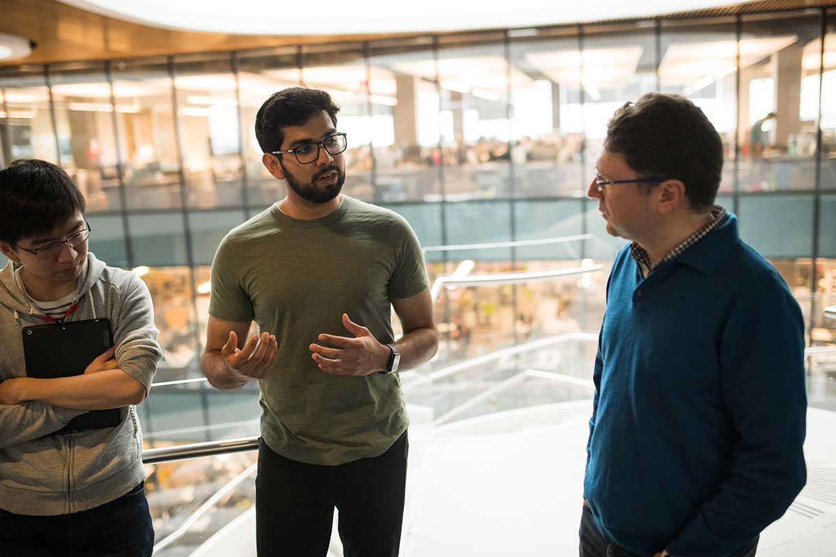 Khoury faculty member Engin Kirda (right) listens to a student, who is standing the middle of a group of three people, talks about his research project.