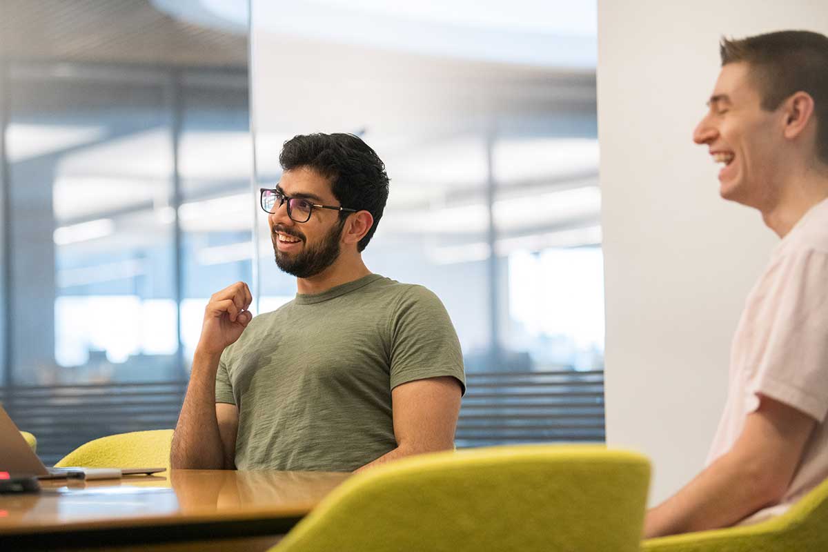 Two Khoury students sitting around a large table laugh during a discussion.