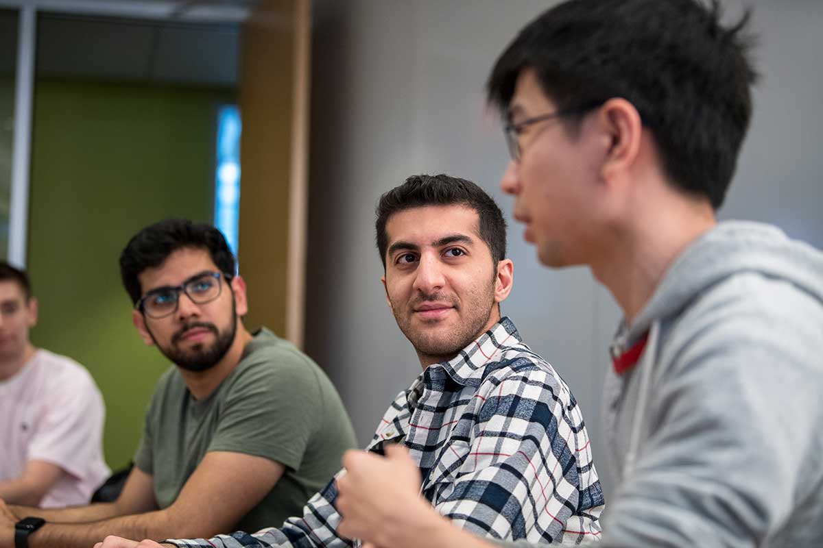 Four Khoury students sit in individual chairs as the student at right speaks. All other students are looking at the speaker.