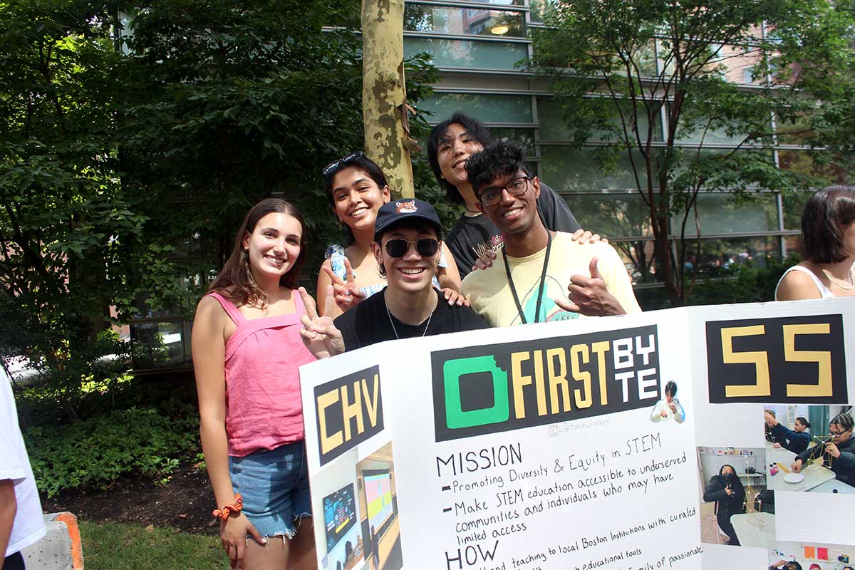 A group of five students stands behind their club's poster at a club fair.