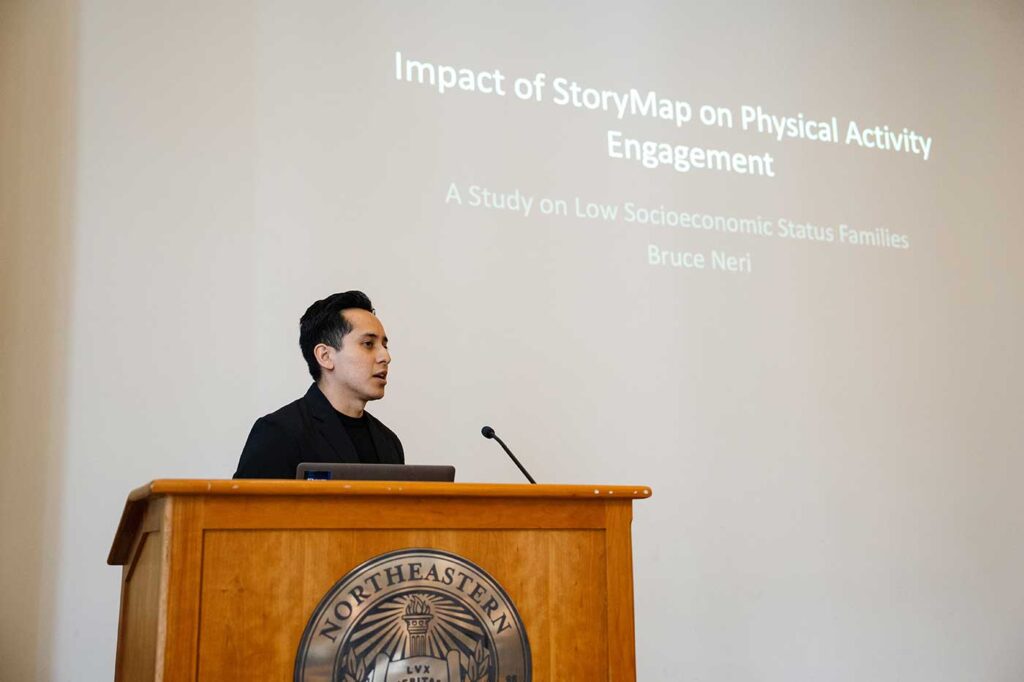 Bruce Neri presents a project while standing behind a podium, with the projection screen visible in the background