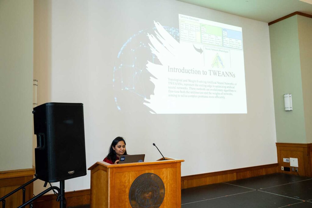 Dilshath Shaik presents a project while standing behind a podium with a large projection screen in the background