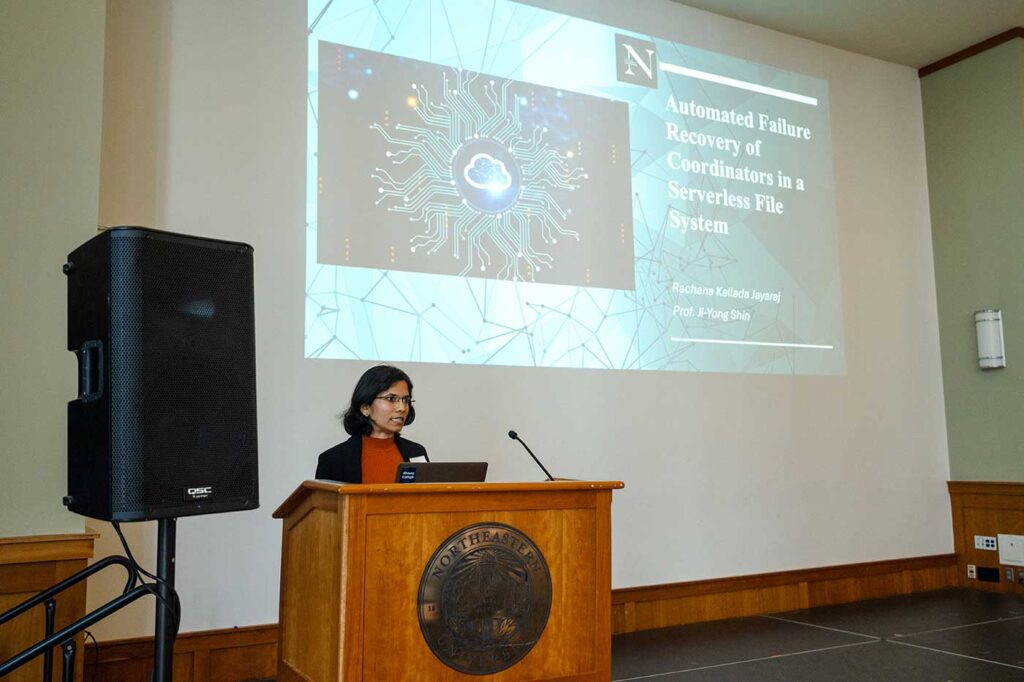 Rachana Kallada Jayaraj presents her project standing behind a podium with the projection screen visible in the background