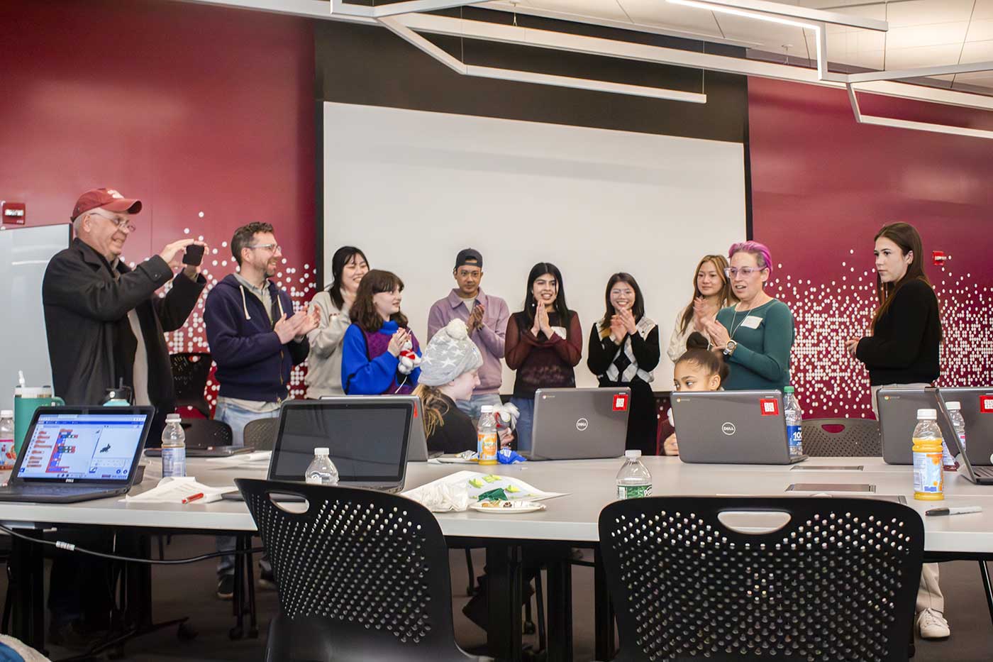 Nine adults stand in the lab applauding for the younger workshop participants