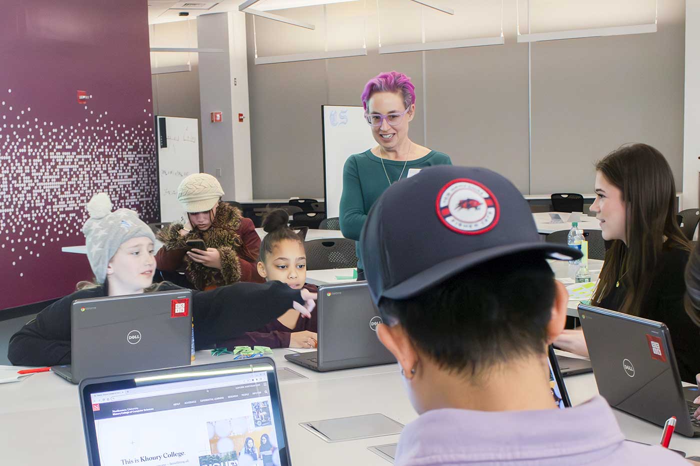 Khoury faculty member Laney Strange stands in the middle of a Khoury lab speaking to a group of students who are seated at tables working on their laptops