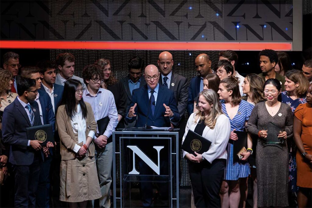 Joseph Aoun speaks at a podium while 2024 Northeastern Awards Convocation winners look on. Photo by Alyssa Stone/Northeastern