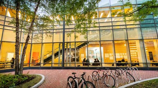 A view of West Village H from an exterior courtyard that shows the building's atrium lit up in yellow light with students sitting at tables