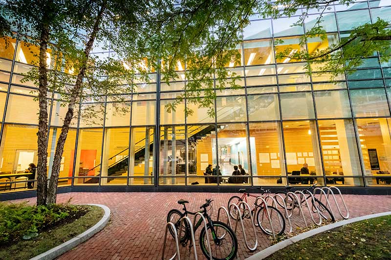 A view of West Village H from an exterior courtyard that shows the building's atrium lit up in yellow light with students sitting at tables