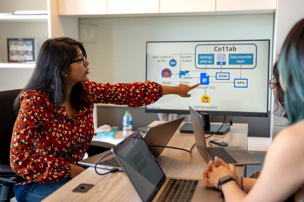 Maitraye Das (left) points at a computer screen while two other researchers look at the screen.