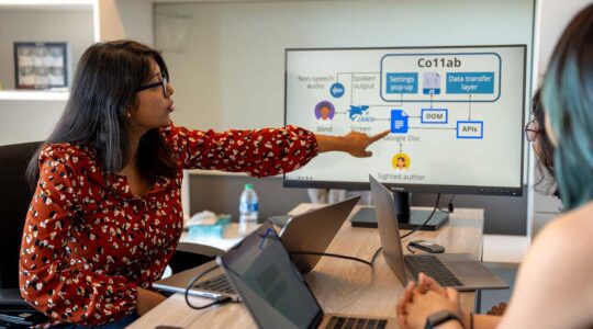 Maitraye Das (left) points at a computer screen while two other researchers look at the screen.