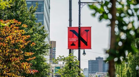 A red banner hanging from a streetlight pole. The banner shows Northeastern's black N wordmark.