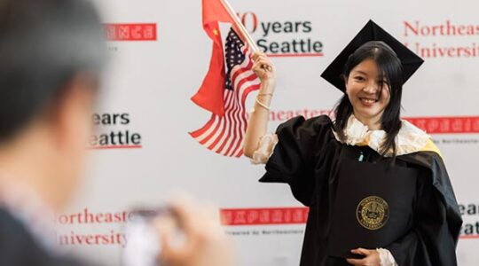 A Northeastern graduate holds small flags of the United States and China in one hand and her diploma in the other hand.