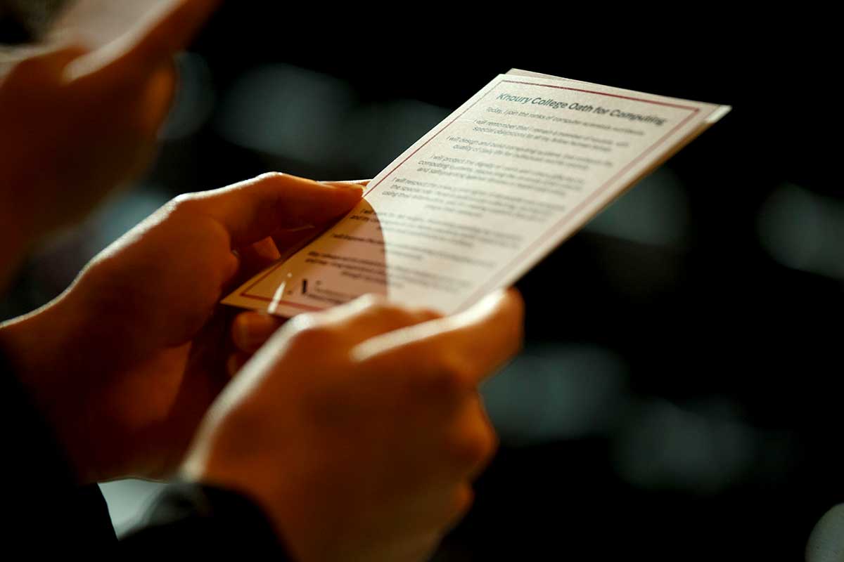 Two hands hold a card that contains the Khoury College Oath for Computing.