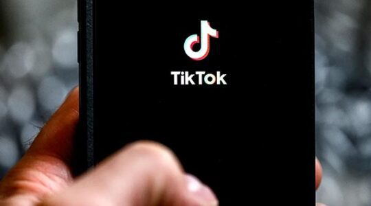 A hand holds a mobile phone with the TikTok logo on the screen.