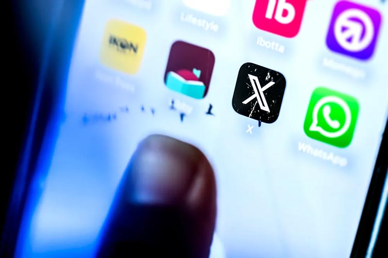 A thumb taps the screen of a mobile device shoing app icons for X, WhatsApp, ibotta and other apps