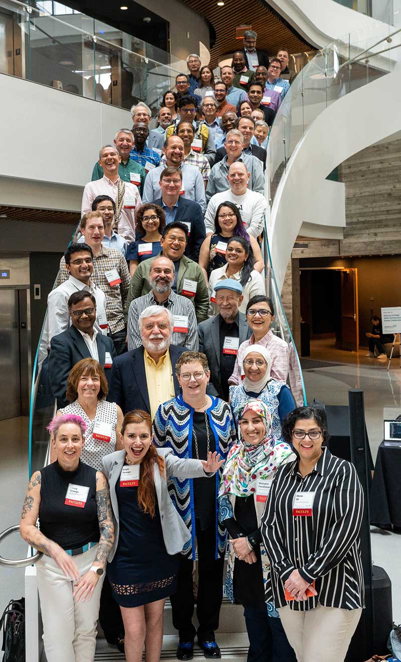 Dozens of Khoury faculty members pose for a photo while standing on the curved staircase in the atrium of Northeastern's ISEC building.