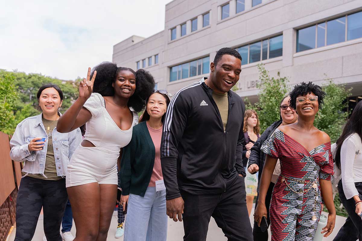 A group of several students smile and laugh while walking by Snell Library at Northeastern's Boston campus