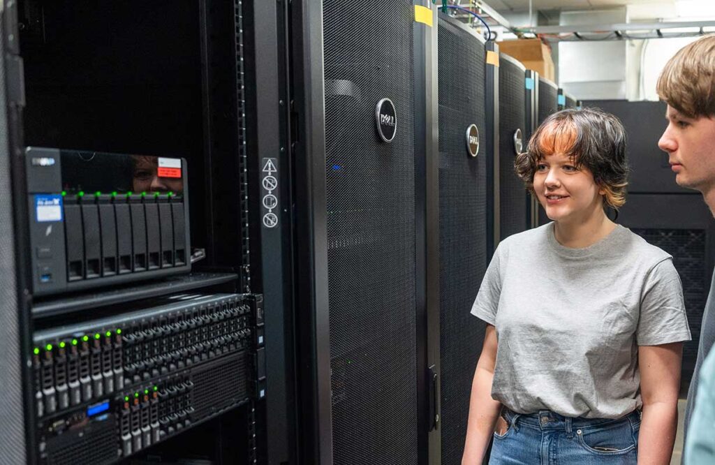 Khoury faculty member Jonathan Bell (right) stands in a server room with two students.