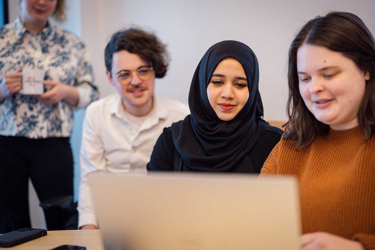 Four Khoury students view and open laptop in a Khoury lab. Three of the students are sitting and the fourth is standing.