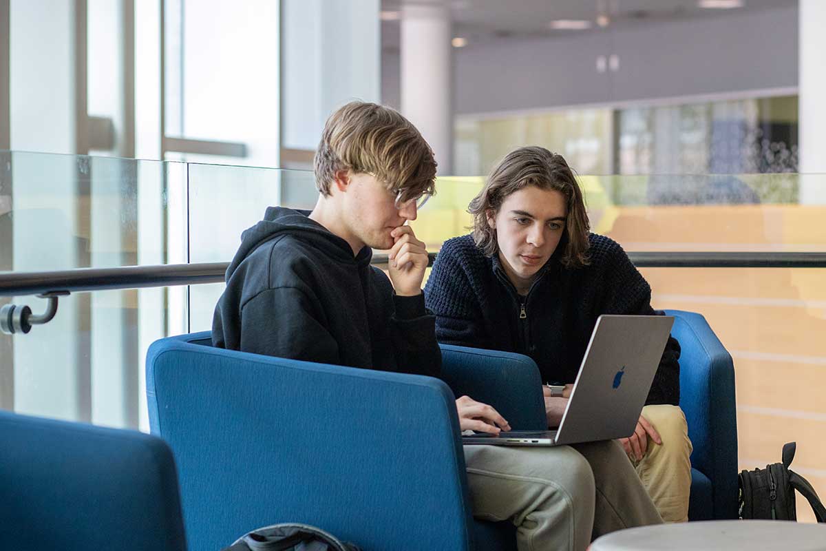 Two students sit in comfortable chairs in a Khoury atrium