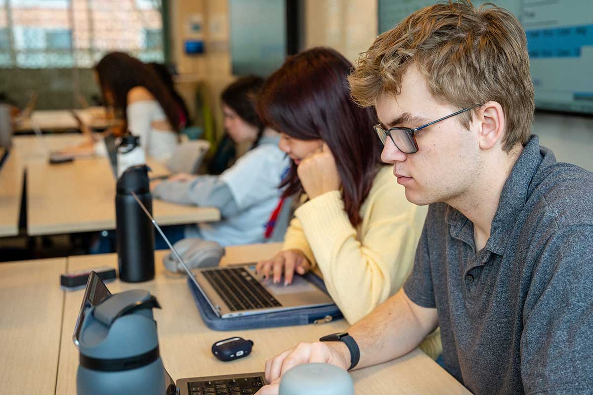 Several students sitting at large, rectangular tables in a Khoury lab type on their laptops