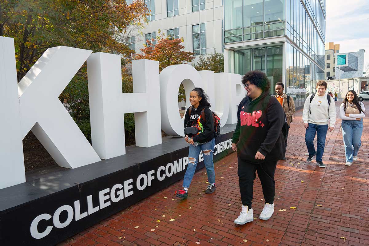 Students walk by a Khoury College sign while walking on a brick sidewalk on Huntington Avenue in Boston