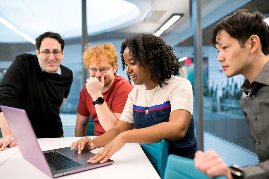 Khoury researchers view a laptop while sitting and standing around a table.