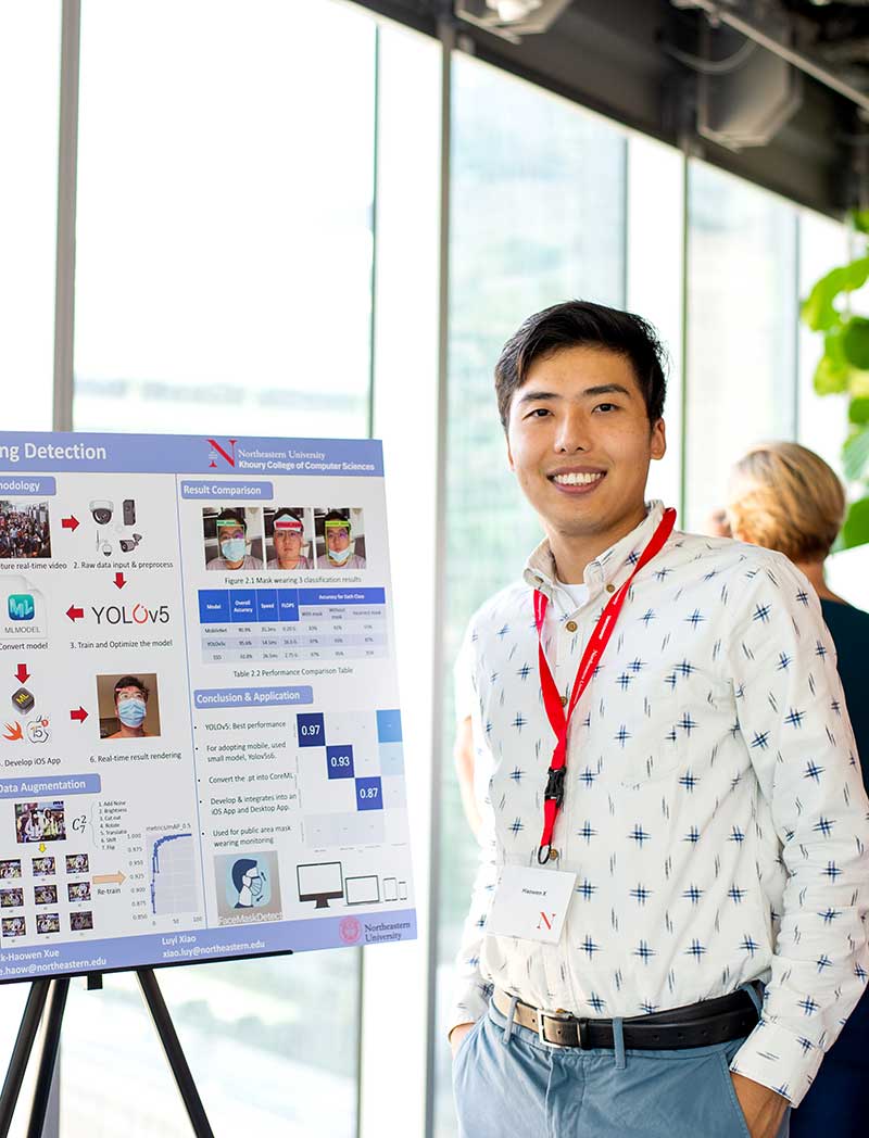 A master's student stands in front of his capstone project poster at a research fair.