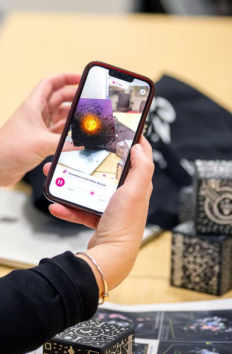 A photo showing a hand grasping a mobile phoe that is showing a video of the formation of the solar system