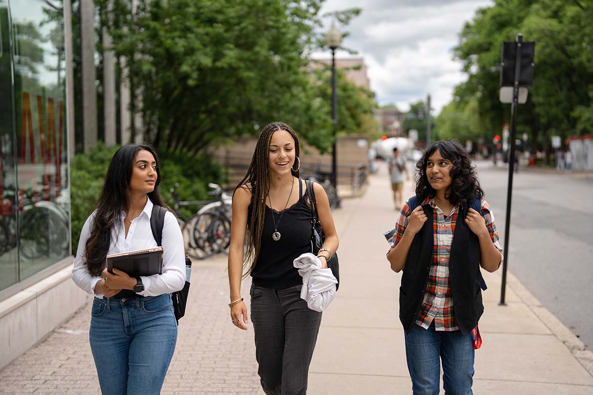 Three students converse while walking on a sidewalk on Northeastern's Boston campus