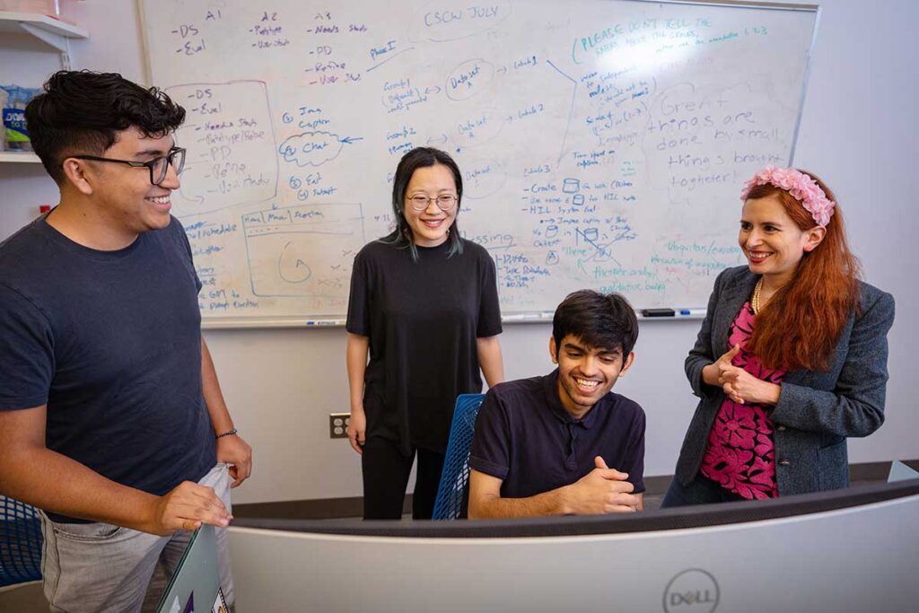 Khoury faculty member Saiph Savage (right) smiles while discussing research with three students in a Khoury lab