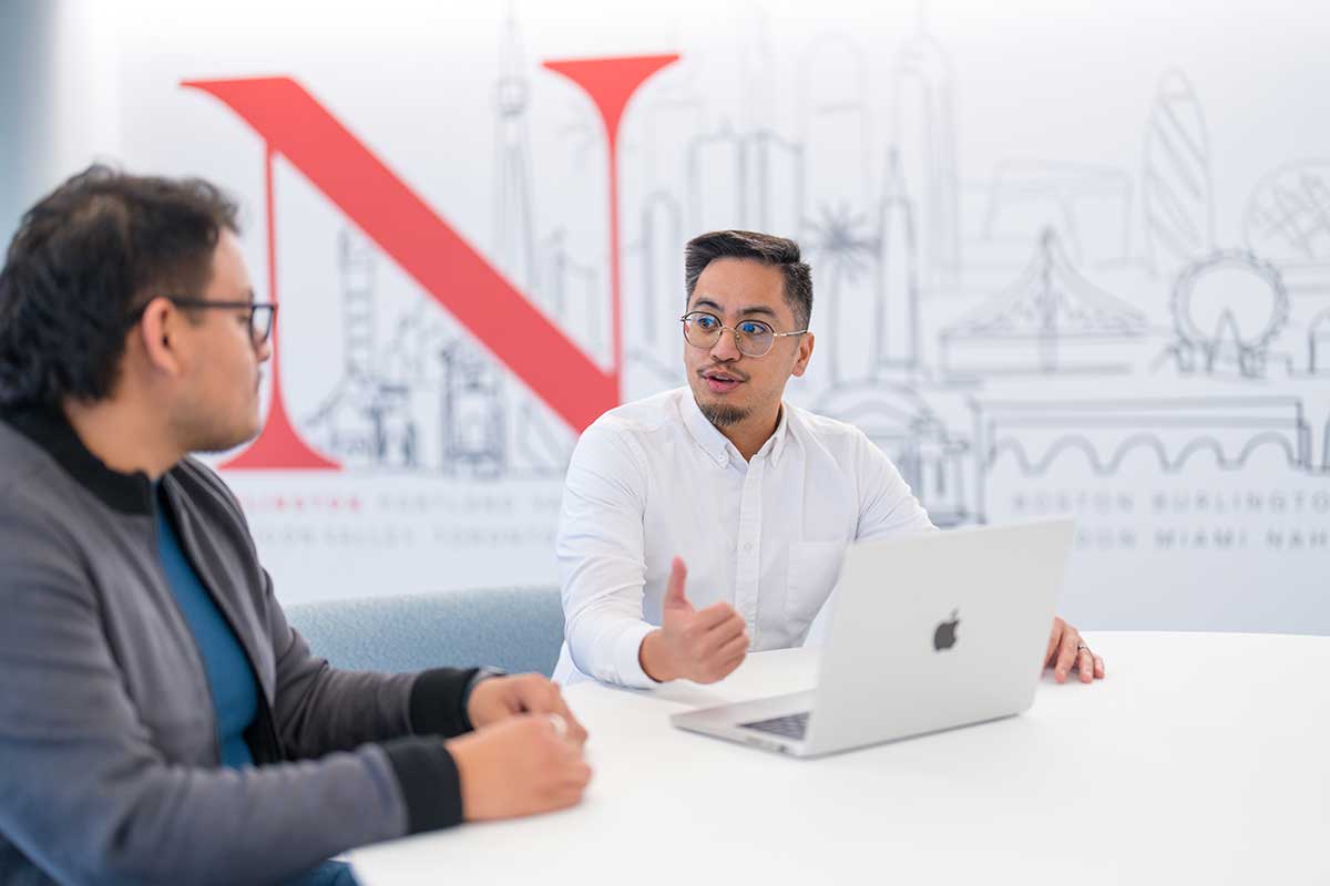 A Khoury staff members speaks with a student while they sit at a white table