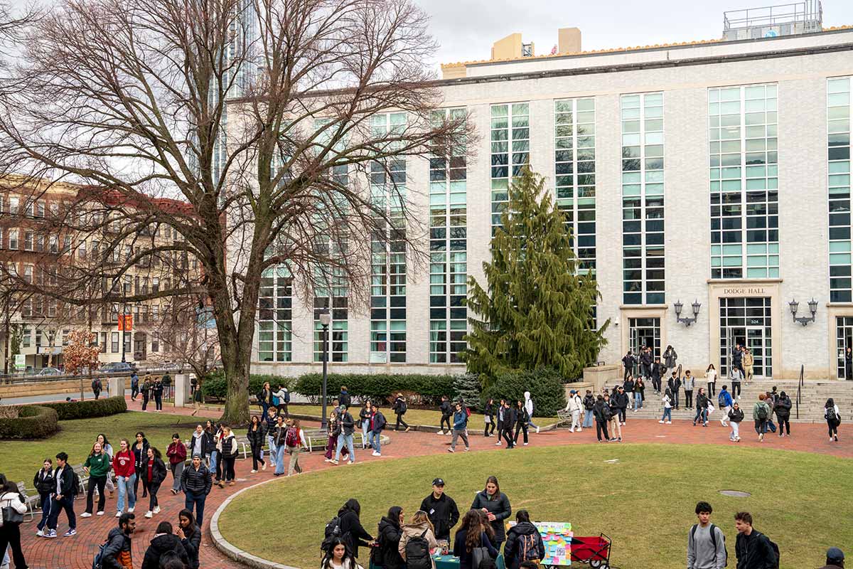 A wide view of Krentzman quad at Northeastern in Boston. Dozens of students are walking on a circular path.