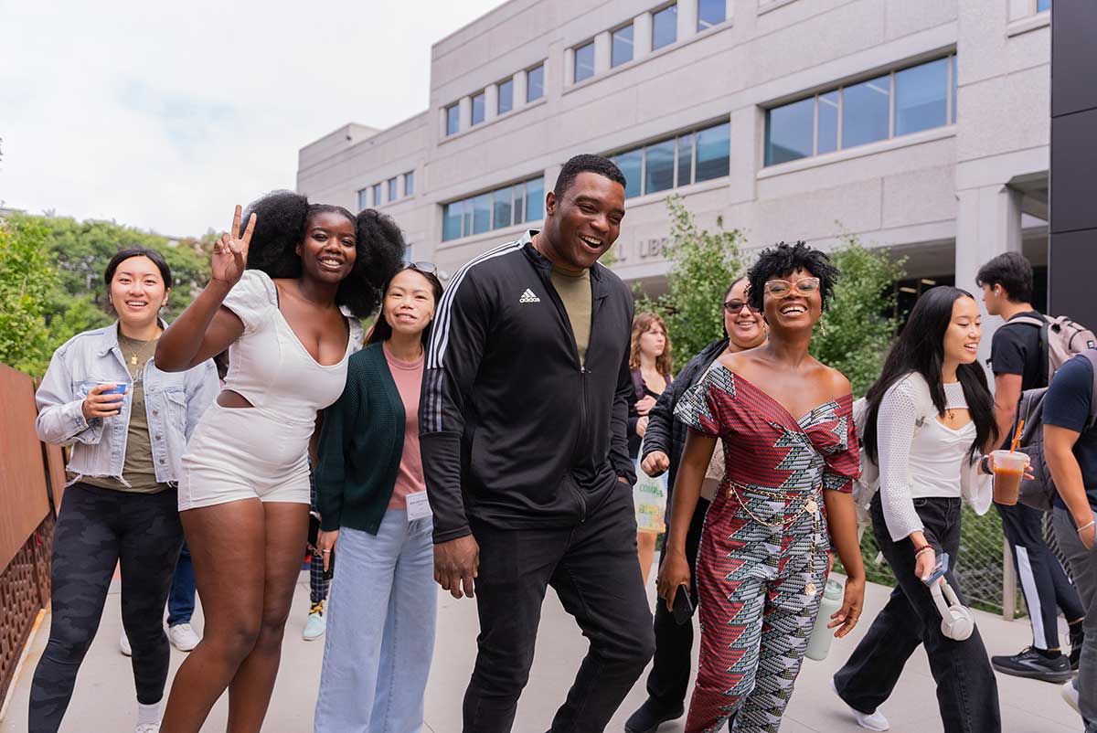 A group of seven students smile and walk through Northeastern's campus