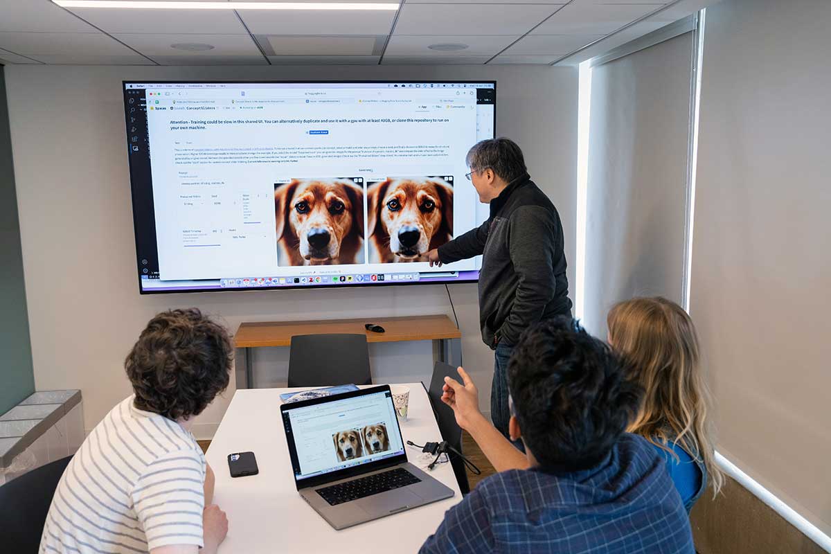 Khoury faculty member David Bau stands and points at a projection screen showing two images of a dog while three students look at the screen