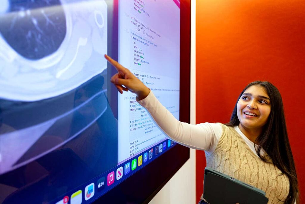 A Khoury student points at a large screen showing an image of a brain in a Khoury conference room