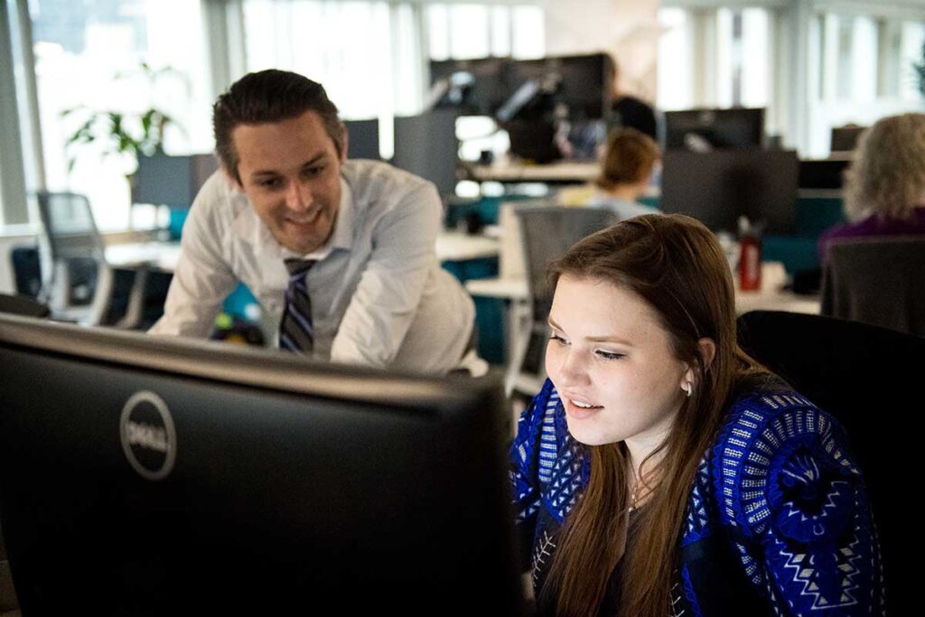 A student works on a computer at a co-op while a colleague stands in the background