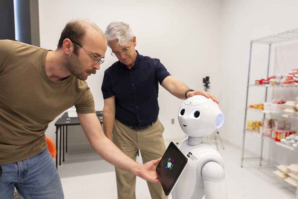 Khoury researchers adjust a white robot shaped like a human with a small display screen hanging on its chest