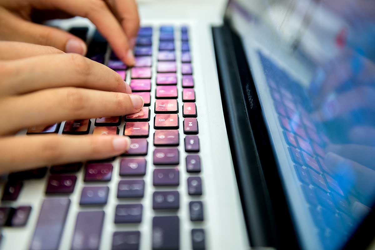 A close-up photo of two hands typing on a laptop's keyboard