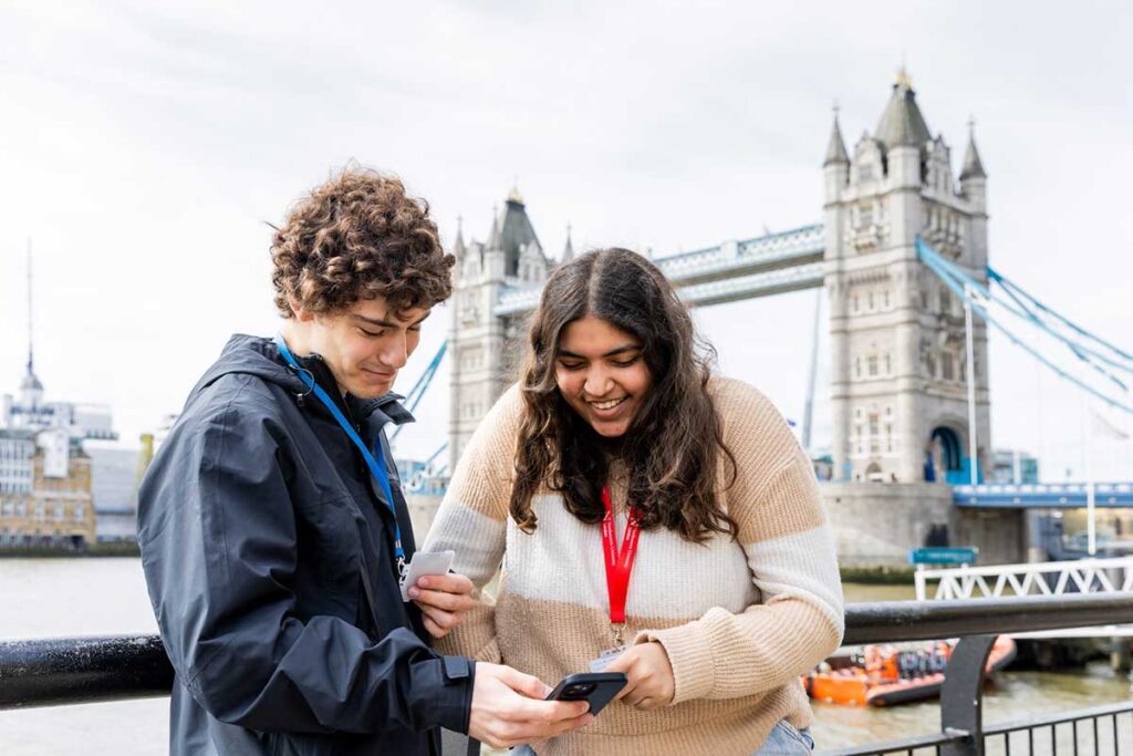 Two students look at a mobile phone at Northeastern's London campus with Tower Bridge in the background