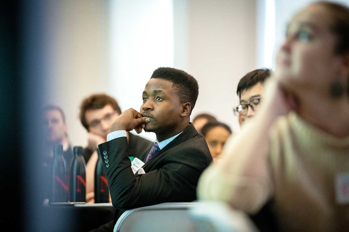 Several students view a presentation in a classroom; the student in the center of the photo has his hand on his chin and is looking attentively