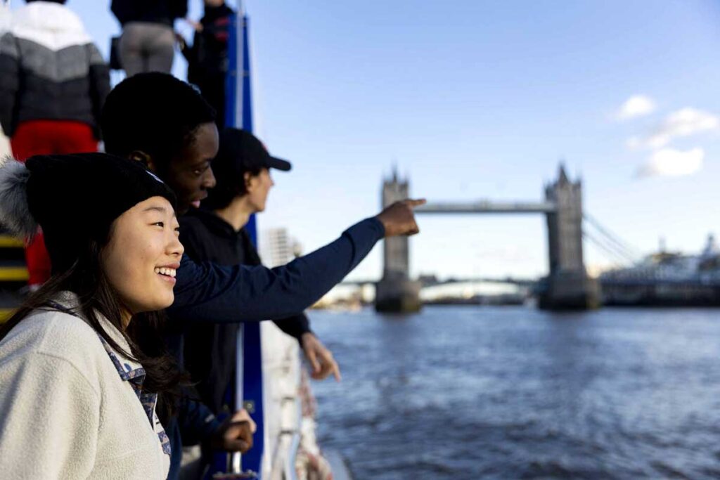 A student standing on the banks of the River Thames in London with Tower Bridge in the background