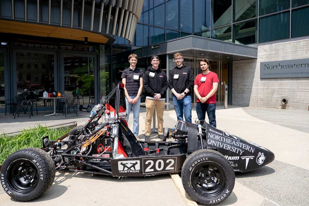 Four members of Khoury's Northeastern Electric Racing team pose for a photo while standing behind their club's race car, which resembles a Formula 1 vehicle.