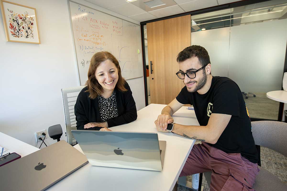 A Khoury faculty member (left) sits on one side of a desk looking at an open laptop while a student sits on the other side of the desk