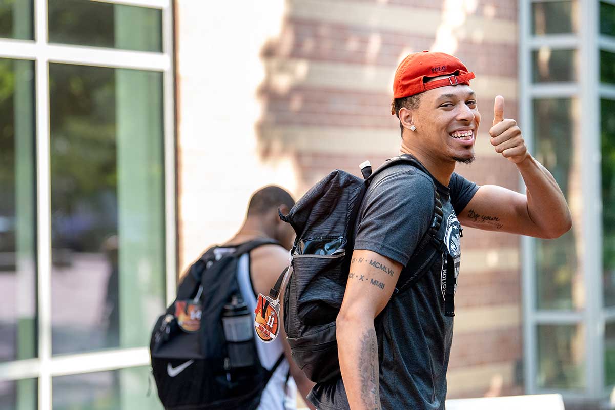 A student walking through Northeastern's Boston campus gives a thumbs up sign