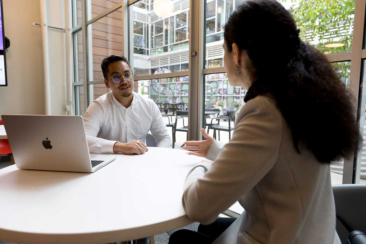 Two Khoury staff members sitting at a round table have a discussion. An open laptop sits on the table.