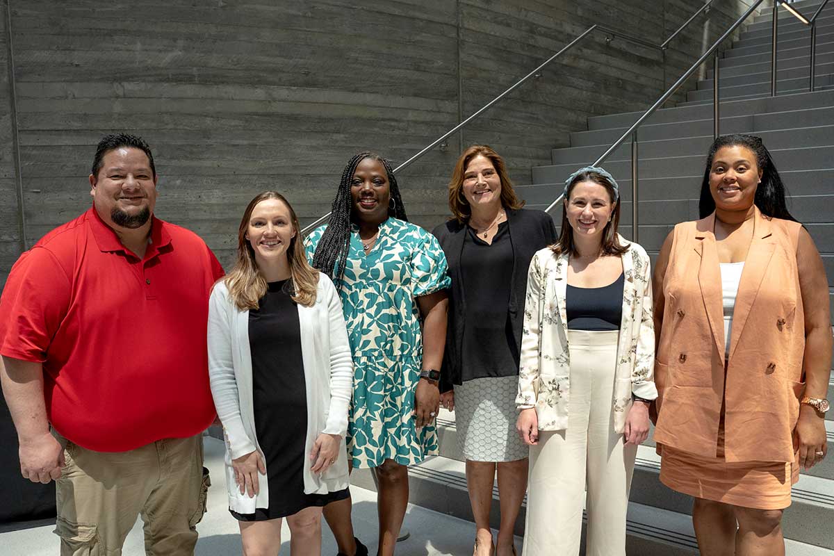 Six Khoury staff members stand outside the ISEC building on Boston's campus. A large staircase is in the background.